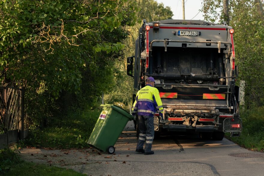 Vīrietis stumj atkrituma konteineri pie auto